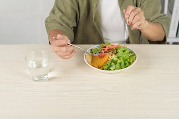 Senior eating fresh vegetable salad with pumpkin and drinking water at home. Elderly healthy lifestyle, organic nutrition, weight loss, and vegetarian diet concept for wellness and healthcare.