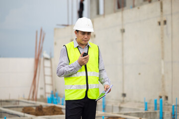 walkie talkie, Asian Man working, Architect or contractor working on house building under construction. Professional Architects Engineer construction site. Civil Engineering in safety harthat helmet