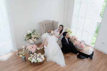 Happy Asian bride and groom in wedding attire, posing indoors with clean background. Stylish groom portrait for wedding photography concept.