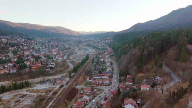 Aerial drone footage of the DN1 road crossing Busteni town, with the Carpathian Mountains surrounding the urban area, filmed during winter daylight in Busteni, Romania.