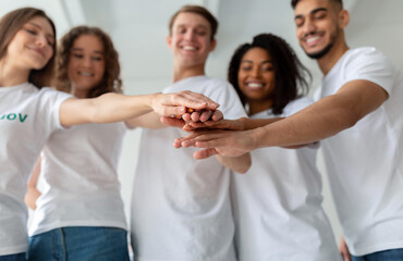 Obraz premium A diverse group of young volunteers stands together, smiling and joining hands, ready to contribute at the charity center. Their teamwork and enthusiasm highlight their collective dedication.