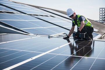 Technician installing solar panels on factory roof for green energy. A skilled technician in safety gear is working on a solar panel installation on rooftop.