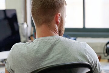 Office worker focused on computer screen, wearing casual attire. Productive workspace setting with modern technology. Ideal for business environments.