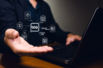 A person holds out a hand displaying digital SEO concepts with a laptop in the background, emphasizing modern marketing techniques and technologies.