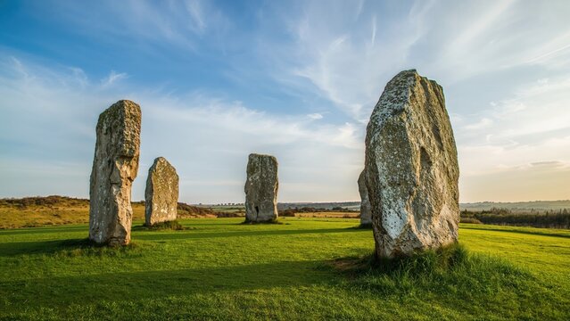 Four standing stones on a green field under a partly cloudy sky.