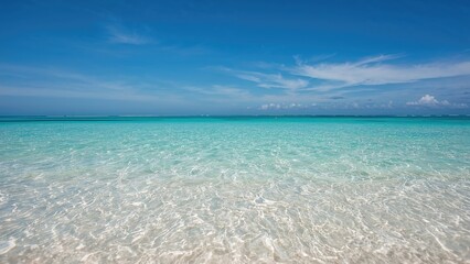 Pristine ocean water with clear, shallow waves and a blue sky, tropical beach scene.