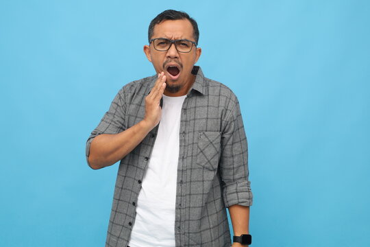 Asian man isolated on blue background, touching his face with expression of suffering from health problems and toothache, standing isolated on blue background.