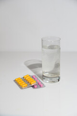 Yellow and pink pills and a glass of water on a white background, space for text.