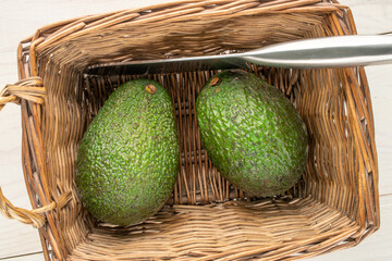 Ripe avocados in a basket on a wooden table, close-up, top view.