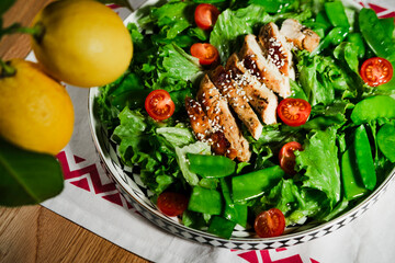 mediterranean styled salad with green lettuce leaves, peas, grilled chicken meat, cherry tomatoes, dressed with olive oil, served for one