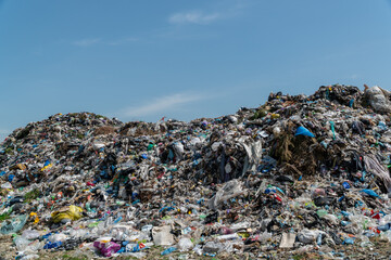 A vast landfill stretches out, overflowing with garbage and plastic waste under a clear blue sky, illustrating serious environmental concerns