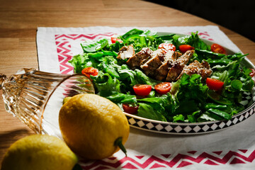 mediterranean styled salad with green lettuce leaves, peas, grilled chicken meat, cherry tomatoes, dressed with olive oil, served for one