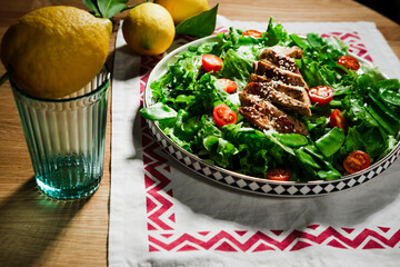 mediterranean styled salad with green lettuce leaves, peas, grilled chicken meat, cherry tomatoes, dressed with olive oil, served for one