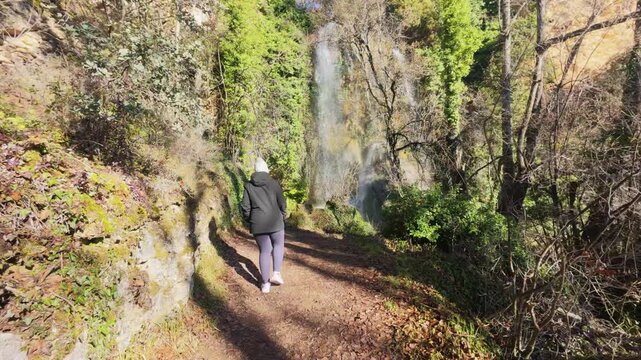 Hiker walking along a forest path with the beautiful Fuentetoba waterfall in the background, enjoying the tranquility of nature during winter in the scenic region of Soria, Castilla y Le&oacute;n, Spain.
