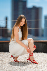 Elegant Woman Posing, Chic Woman With Flowing Hair Dressed In White On Urban Rooftop Adjusting Vibrant Heels