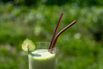 Glass of green smoothie on nature background. Healthy organic drink made from banana, dill, parsley, cucumber and avocado