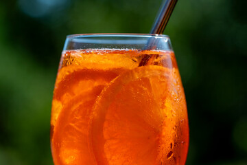 Aperol spritz cocktail in wine glass on a nature background. Classic italian aperitif aperol spritz cocktail with orange and ice cubes. Closeup. Summer refreshing drink with sunlight