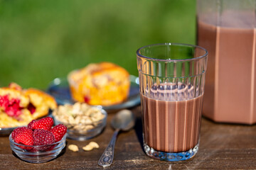Indian masala chai or tea or cacao in glass with jug and raspberry muffin on the table in cafe on nature background, close up. Trendy healthy drink