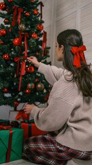 Woman decorating a Christmas tree with red ornaments and ribbons, surrounded by gifts