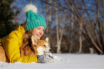Obraz premium Woman hugging corgi on snow in winter park with copy space on sunny day