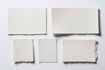 Five pieces of handmade white textured paper with torn edges on a plain background.