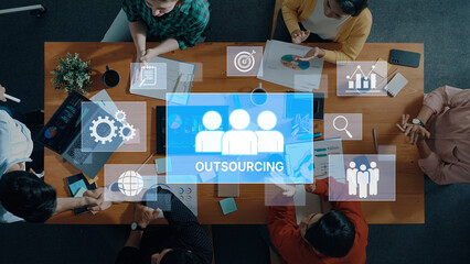 A diverse business team engages in a meeting focused on outsourcing strategies, utilizing digital tools and data visualization in a modern office environment. Trope