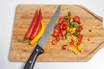 Whole and sliced chili peppers with a kitchen knife on a wooden cutting board. Spicy cooking preparation scene.