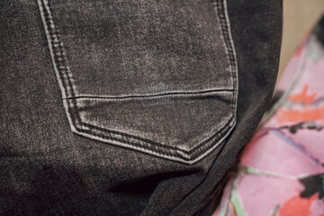 Close-up of a black denim fabric showing a pocket with subtle wear and texture, set against a colorful background. Ideal for fashion and textile marketing applications.