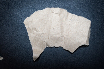 A crumpled piece of brown paper rests on a dark surface. This image captures the texture and form of the paper, ideal for concepts related to recycling, creativity, or stationery.