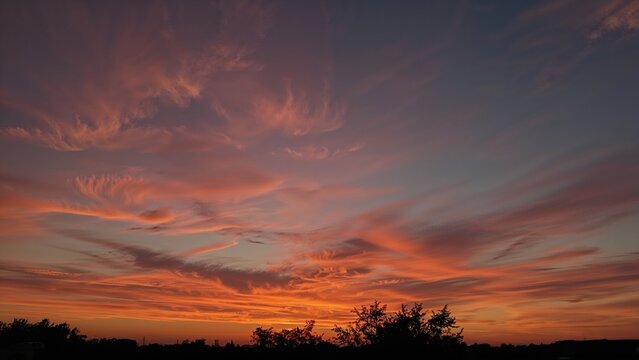 Colorful sunset sky with clouds and silhouetted trees.