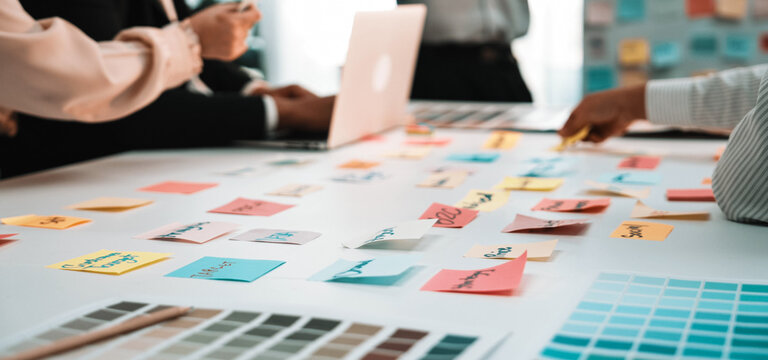 A dedicated team engages in a brainstorming session, utilizing sticky notes and laptops in a modern office environment to drive creativity and project planning. SACTR - Powered by Adobe