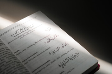 Macro shot of open Quran pages featuring beautiful Arabic calligraphy and Indonesian translation, highlighted by a soft beam of natural light for a spiritual and educational concept