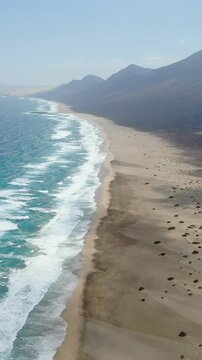 Aerial view of Cofete beach in Fuerteventura. Stunning aerial perspective of turquoise waves crashing on a vast, empty sandy shoreline