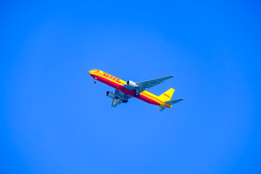 Florida, United States - Jan 01, 2025: Yellow Cargo Plane With Red Stripes With Shipping Mailing Service Logo On Hull Seen In The Sky With Landing Gear Down