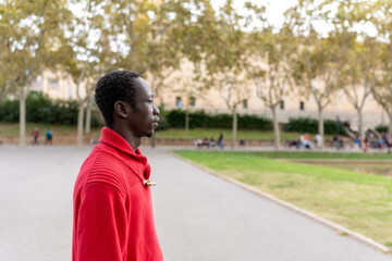 African man wearing a red sweater and looking forward, enjoying a moment in a city park