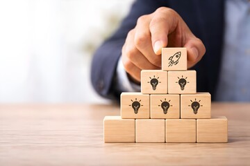 Businessman places a rocket icon block atop a pyramid of idea blocks signifying startup launch and innovation achievement