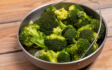 A steamer with steamed broccoli florets on a wooden table. Healthy vegan food preparation concept.
