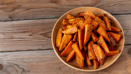 A plate with sweet potatoes roasted with thyme. Rustic wooden background with copy space.