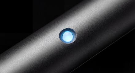 This close-up image showcases a modern black device featuring a glowing blue button, highlighting its sleek design and technological sophistication, set against a dark background for contrast