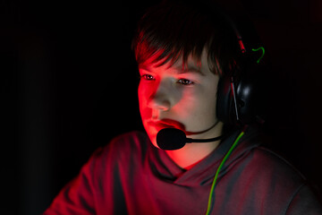 Young male gamer wearing headset, focused on screen in dark environment, illuminated by red light, showcasing intense concentration and engagement in gaming experience