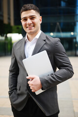Businessman poses with laptop outside office building