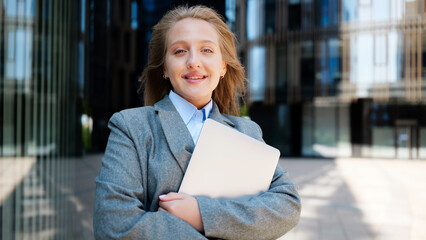 Businesswoman stands outside modern building with laptop