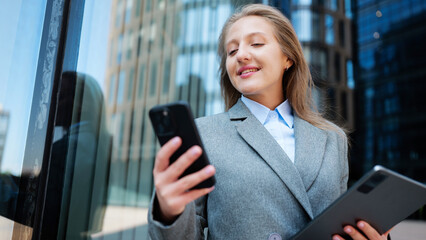 Woman using mobile phone and tablet outside a building