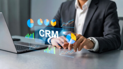 Businessman interacting with holographic crm interface showing business analytics and data charts next to a laptop in an office setting