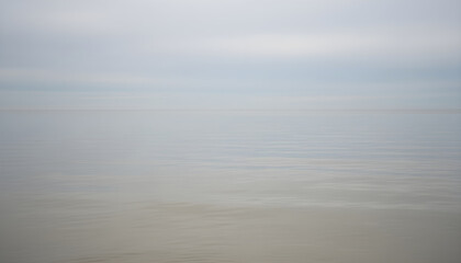Calm ocean water meeting foggy horizon sky
