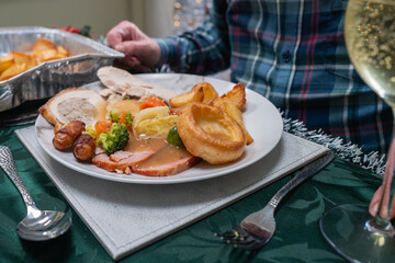 Small sausages wrapped in bacon on a Christmas dinner plate with vegetables, turkey and gammon. There is also a Yorkshire pudding and roast potatoes. The table cloth is green. 