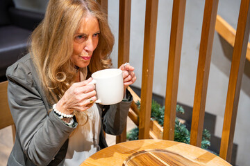 Woman enjoys a warm beverage in a cozy cafe setting while relaxing in a wooden chair on a calm afternoon