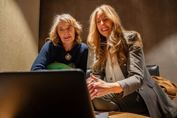 Two women sharing ideas while working together in a cozy, dimly lit office space during an afternoon meeting