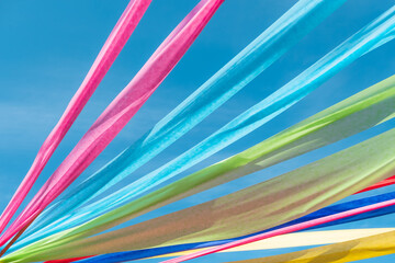 Low angle view of colorful fabric ribbons waving in the wind against blue sky during summer festival celebration