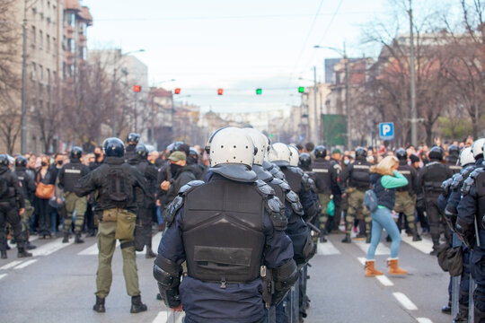 Riot police line in winter city street protest, crowd control and public demonstration security with blurred protesters in background
